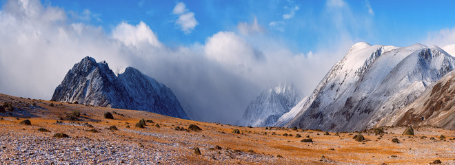 Majestic snow peaks in the clouds panorama.