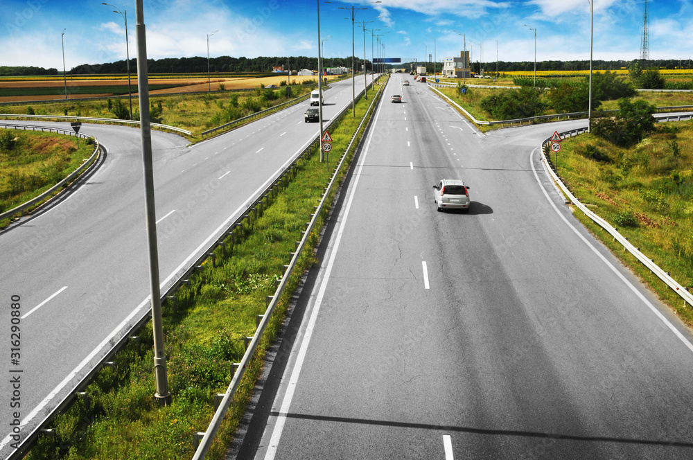 Wall mural Cars on the countryside road with fields and trees against blue sky with clouds