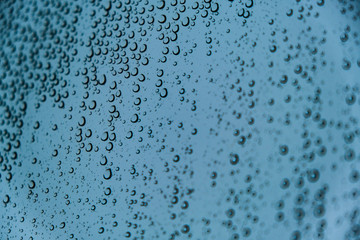 Raindrops on Transparent Glass Surface on a Cold Snowy Winter Background