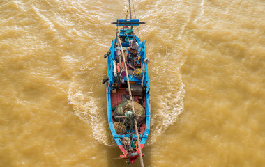 A small fishing wood boat is sailing in the sea for fishing. The photo was taken from above. Brown seawater due to the recent typhoon and many river sediment.