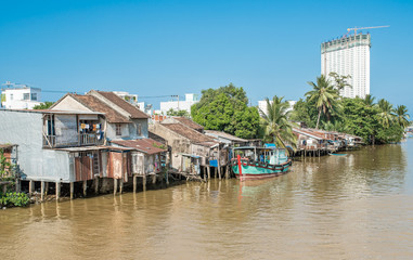 Fishing village in Nha Trang city, Vietnam. Shacks houses stand on stilts in the water on the waterfront. A fishing boat anchored near one of the houses. A modern skyscraper in the distance.
