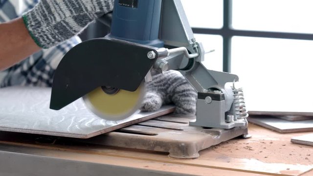 4K Close up shot of Asian construction technician man hands wearing glove using tile cutting machine cut large gray ceramic tile for renovation home repair in workshop. Handyman diy working concept.