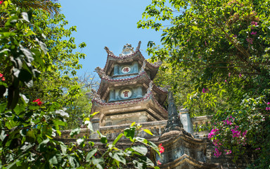 Buddhist pagoda hidden among trees and bushes. Pagoda against the blue sky surrounded by greenery. Vietnam.