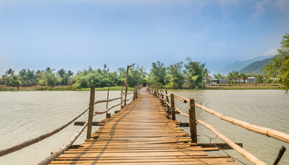 First-person view of a wooden and not safe railing bridge over the river in Vietnam.