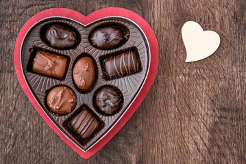 Simple heart shaped box of chocolate Valentine’s Day candy on a wood table, with a wood heart