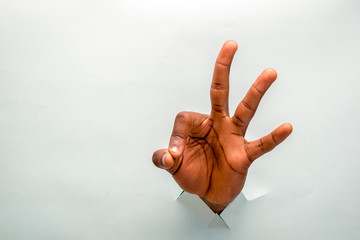black person hand through a hole in a cardboard making ok sign, showing three fingers