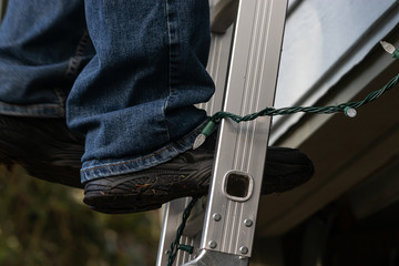 mans black shoes standing on silver ladder with christmas lights