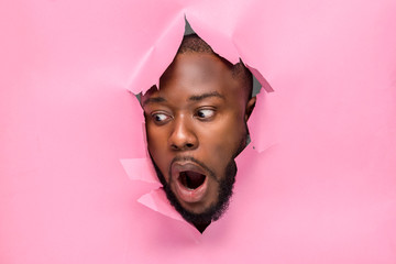 handsome young black man with head through a cardboard paper surprised and looking downwards
