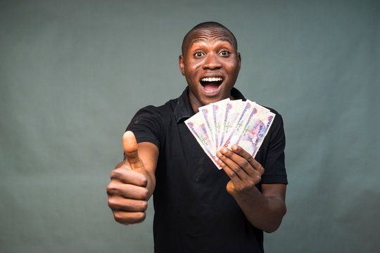 young african man holding some cash, feeling excited and happy, doing thumbs up