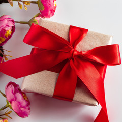 Gift box with red ribbon and flowers on a white background.