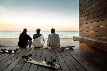 Three young boys watching the sunset on the beach next to their skateboards