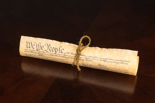 The U S Constitution Rolled  Tied With Cord Displaying We The People On An Oak Table With Reflection