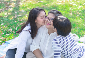 Fototapeta premium Asian lovely young daughter and grandson kiss happy and healthly senior woman or pleasure grandmother in moment of beautiful love in the park. Family generation relationship or bonding photo concept