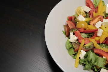 Salad of vegetables in a white plate close-up on a dark background