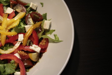 Salad of vegetables in a white plate close-up on a dark background