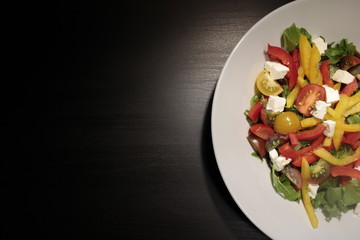 Salad of vegetables in a white plate close-up on a dark background