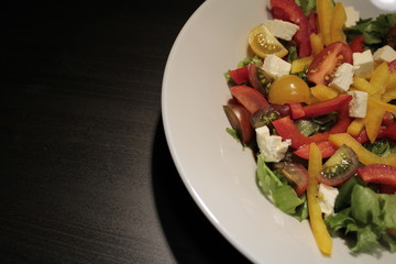 Salad of vegetables in a white plate close-up on a dark background