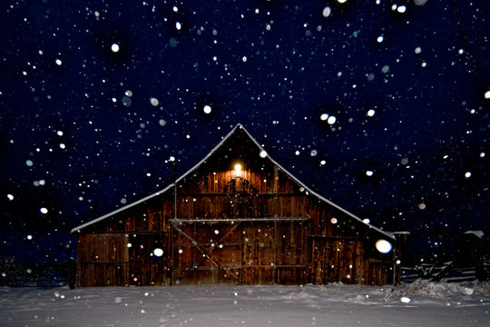 A peaceful snow scene with Old Rustic Barn with peak light and falling snow at night, Eastern Oregon 