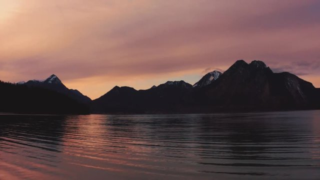 Anamorphic 4K Aerial Drone footage of the famous and scenic and idyllic Bavarian lake Walchensee in southern Germany in the alps. The sunset is coloring the clouds above the snowy mountain tops red.