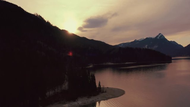 Anamorphic 4K Aerial Drone footage of the scenic and idyllic Bavarian lake Walchensee in southern Germany in the alps. The sunset is coloring the clouds above the snowy mountain tops red.