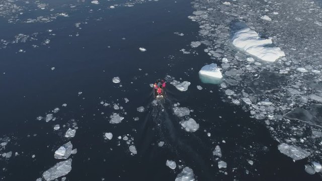 Motor boat floats among the Antarctic ice floes and icebergs. Aerial tracking drone flight overview of south pole ocean landscape. Rubber boat sailing in open water brash ice. Footage shot in 4K (UHD)