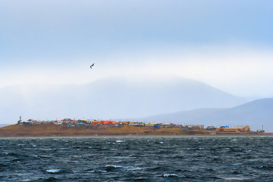 View from the sea to the Chukchi village of Yanrakynnot, located on the shores of the Senyavin Strait of the Bering Sea, surrounded by tundra and mountains. Autumn rainy weather. Chukotka, Russia.