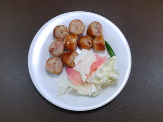 Top view of Thai Sausages with cabbage, pickled ginger and pepper on white plate isolated on wooden table as a background, Ready to eat, Space for text in template (Sai Krok Isan)