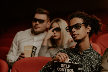 Multiethnic friends with popcorn watching movie in cinema