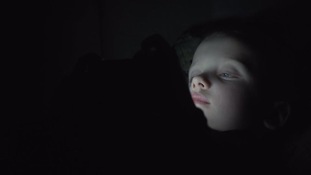7 years old child boy using smartphone at night in bed