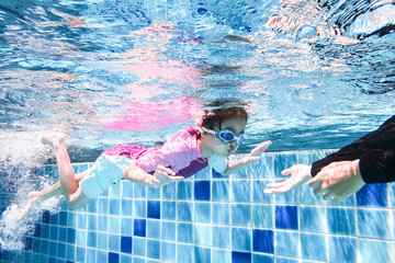 Underwater young little cute girl is swimming in the swimming pool with her swimming teacher. Seen...