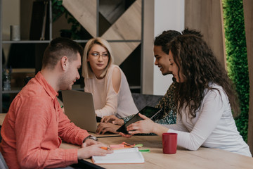 Fototapeta premium Diverse group of smiling young designer working together over a laptop during a meeting in the boardroom of a modern office