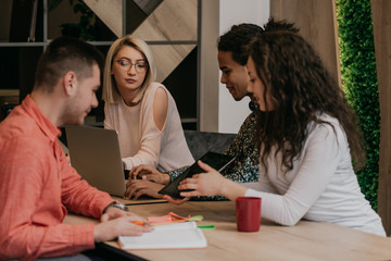 Diverse group of smiling young designer working together over a laptop during a meeting in the boardroom of a modern office