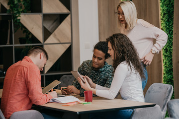 Obraz premium Diverse group of smiling young designer working together over a laptop during a meeting in the boardroom of a modern office