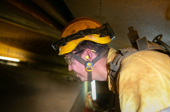 Closeup Construction Worker Wearing Safety Helmet, Clear Glass Ears Noise Protection Headlamp While Performing Working Inside Confined Spaces