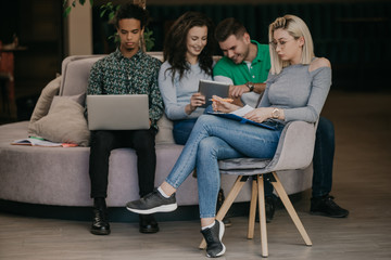 Obraz premium Diverse group of smiling young designer working together over a laptop during a meeting in the boardroom of a modern office