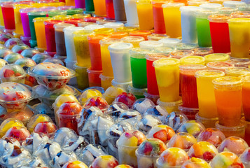 Fototapeta na wymiar Multicolour background of fresh smoothie and fruits cutted into pieces in plastic cups, close up view. Selective soft focus. Blurred background