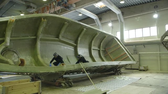 Fiber glass molding  workers with masks - wide angle camera dolly movement to the right- boat parts factory of off shore life boats - Norway