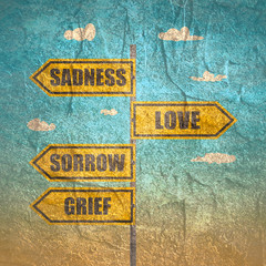 Road signs with sadness, sorrow, grief and love words pointing in opposite directions.