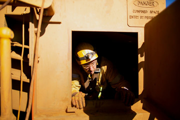 Wide angle shot of male rope access technician maintenance worker wearing safety harness, helmet egress out from confined space restricted area entry door construction site, Sydney, Australia  