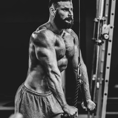 Fototapeta na wymiar Handsome strong sportsman training in gym and doing pull-ups, dramatic black and white image