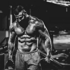Fototapeta na wymiar Portrait of strong handsome fit man exercising in gym with dumbbells, dramatic black and white image