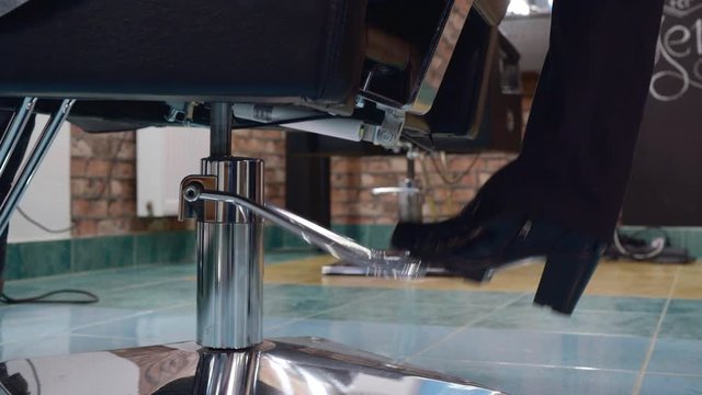 Cropped shot of person pushing pedal on chair in barber shop. Close-up partial view of hairdresser lifting chair and pushing pedal with foot in hair salon