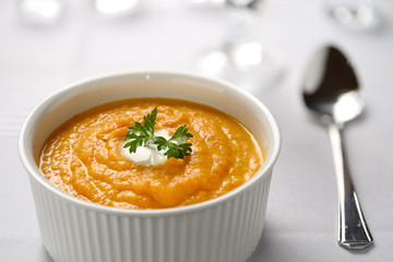 Carrot soup with cream and parsley in white bowl with white tablecloth