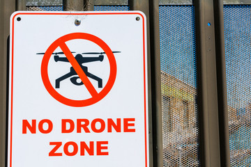 No drone zone warning sign on perimeter fence wall