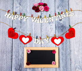 Happy Valentines Day with red hearts and flowers on a wood background with copy space on a chalkboard