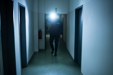 Fototapeta premium Security Guard With Flashlight In Building Corridor