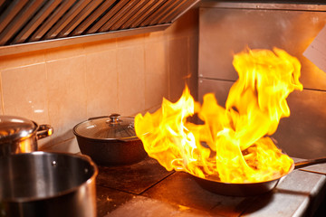Flambe. Fire in frying pan. Professional chef in a commercial kitchen cooking. Man frying food in...