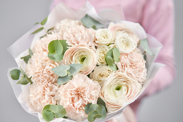 Persian buttercup in womans hands. Bunch pale pink ranunculus flowers with green eucalyptus. The work of the florist at a flower shop