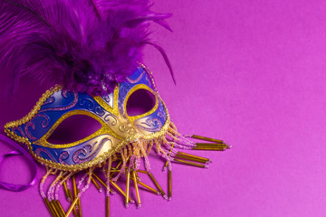 Carnivale mask with purple feathers on a purple background.