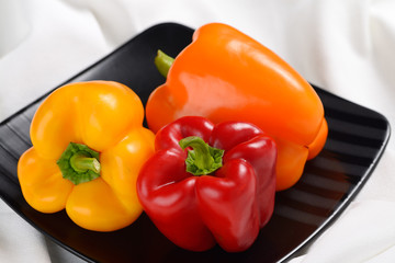 Red yellow and orange bell peppers on a square black plate
